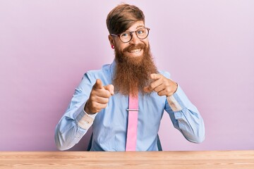 Canvas Print - Young irish redhead man wearing business shirt and tie sitting on the table pointing fingers to camera with happy and funny face. good energy and vibes.