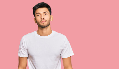 Young handsome man wearing casual white tshirt relaxed with serious expression on face. simple and natural looking at the camera.