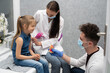 © fotodrobik - A nurse is getting ready to inject a little girl with a previously prepared vaccine. The young apprentice tries to talk to the child so that she is not afraid of the injection.