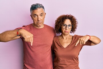 Poster - Beautiful middle age couple together wearing casual clothes pointing down looking sad and upset, indicating direction with fingers, unhappy and depressed.