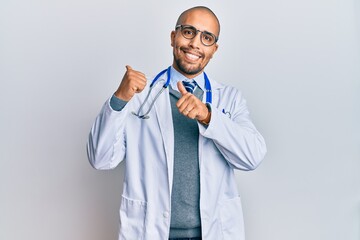 Canvas Print - Hispanic adult man wearing doctor uniform and stethoscope pointing to the back behind with hand and thumbs up, smiling confident