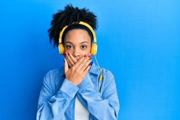 Wall Mural - Young african american girl listening to music using headphones shocked covering mouth with hands for mistake. secret concept.