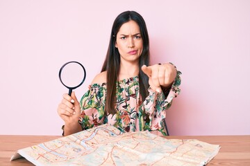 Sticker - Young caucasian woman sitting at the desk searching on city map using magnifying glass pointing with finger to the camera and to you, confident gesture looking serious