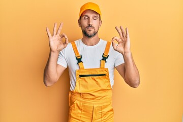 Poster - Young handsome man wearing handyman uniform over yellow background relaxed and smiling with eyes closed doing meditation gesture with fingers. yoga concept.