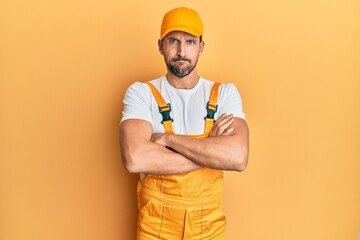 Poster - Young handsome man wearing handyman uniform over yellow background skeptic and nervous, disapproving expression on face with crossed arms. negative person.