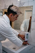 © Denis - Morning procedures in the bathroom. A young man in a white coat stands at the mirror. Problem skin and care for it. Non-standard appearance.