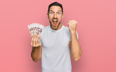 Wall Mural - Handsome man with beard holding 50 mexican pesos banknotes screaming proud, celebrating victory and success very excited with raised arms