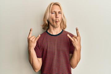 Sticker - Caucasian young man with long hair doing rock gesture making fish face with mouth and squinting eyes, crazy and comical.