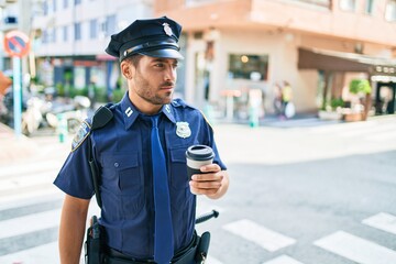 young hispanic policeman wearing police uniform with serious expression. drinking cup of take away c