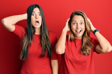 Poster - Hispanic family of mother and daughter wearing casual clothes over red background crazy and scared with hands on head, afraid and surprised of shock with open mouth