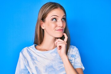 Wall Mural - Young blonde girl wearing casual clothes thinking concentrated about doubt with finger on chin and looking up wondering