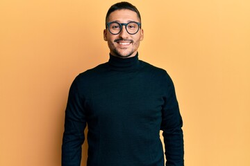 Wall Mural - Handsome man with tattoos wearing turtleneck sweater and glasses with a happy and cool smile on face. lucky person.