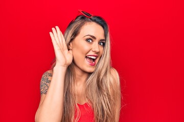 Sticker - Young beautiful blonde woman wearing red t-shirt and sunglasses over isolated background smiling with hand over ear listening and hearing to rumor or gossip. Deafness concept.