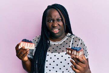 Poster - Young black woman with braids holding cheesecakes clueless and confused expression. doubt concept.