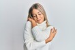 © Krakenimages.com - Beautiful blonde woman wearing casual turtleneck sweater hugging oneself happy and positive, smiling confident. self love and self care
