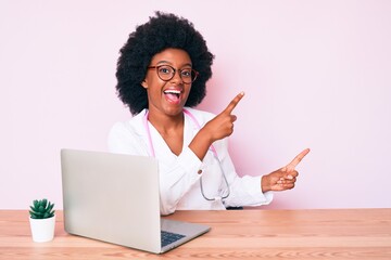 Poster - Young african american woman wearing doctor stethoscope working using computer laptop smiling and looking at the camera pointing with two hands and fingers to the side.