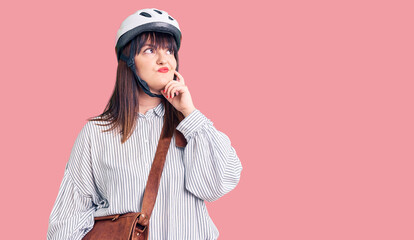 Sticker - Young plus size woman wearing bike helmet and leather bag serious face thinking about question with hand on chin, thoughtful about confusing idea