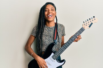 African american woman playing electric guitar smiling and laughing hard out loud because funny crazy joke.