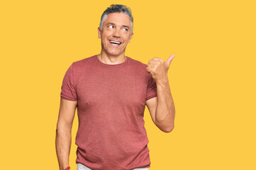 Poster - Handsome middle age man wearing casual clothes smiling with happy face looking and pointing to the side with thumb up.