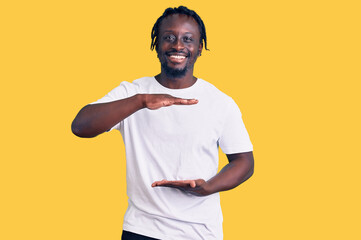 Poster - Young african american man with braids wearing casual white tshirt gesturing with hands showing big and large size sign, measure symbol. smiling looking at the camera. measuring concept.