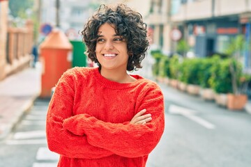 Young hispanic woman with arms crossed smiling happy at the city.