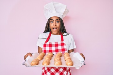 Poster - Young african american woman with braids wearing baker uniform holding homemade bread celebrating crazy and amazed for success with open eyes screaming excited.