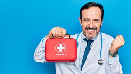 Middle age handsome doctor man wearing coat and stethoscope holding first aid kit screaming proud, celebrating victory and success very excited with raised arm