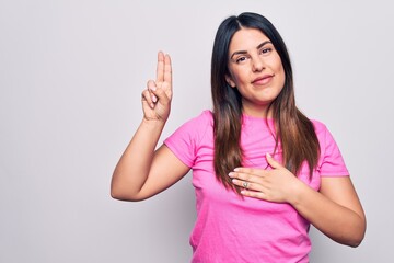 Poster - Young beautiful brunette woman wearing casual pink t-shirt standing over white background smiling swearing with hand on chest and fingers up, making a loyalty promise oath