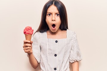 Sticker - Beautiful child girl holding ice cream scared and amazed with open mouth for surprise, disbelief face