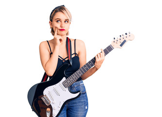 Young beautiful blonde woman playing electric guitar serious face thinking about question with hand on chin, thoughtful about confusing idea