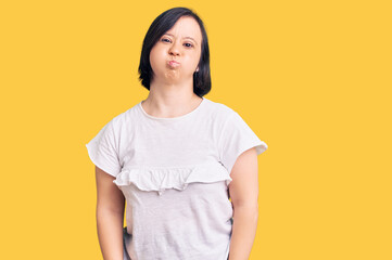 Wall Mural - Brunette woman with down syndrome wearing casual white tshirt puffing cheeks with funny face. mouth inflated with air, crazy expression.