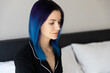 Beautiful woman with blue hair in black nightwear sitting on bed after sleep