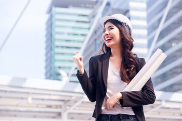 Portrait of Happy professional construction engineer woman holding the blueprint and wearing the safety helmet and glasses at the building site place background,