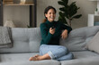 © fizkes - Overjoyed millennial Caucasian woman sit relax on sofa in living room enjoy cozy domestic weekend. Happy young 20s female rest on couch at home laugh watching TV program. Entertainment concept.