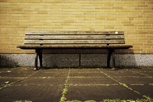 Low Angle View Of Empty Park Bench Against Yellow Brick Wall