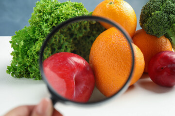 Wall Mural - woman with magnifying glass exploring vegetables and fruits, closeup. poison detection