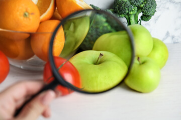 Wall Mural - woman with magnifying glass exploring vegetables and fruits, closeup. poison detection
