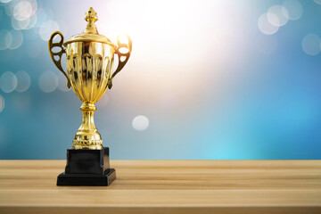 1st champion award, the best prize and winner concept, championship cup or winner trophy on wood table with soft blue and bokeh background