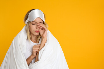 Sticker - Young woman in sleeping mask wrapped with soft blanket on yellow background. Space for text