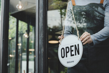 asian waitress staff woman wearing apron turning open sign board on glass door in modern cafe coffee shop, hotel, cafe restaurant, retail store, small business owner, food and drink concept