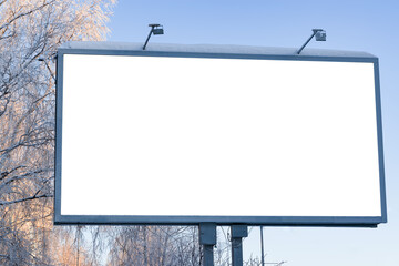 Billboard on the street in the city with an empty white space for text on a background of trees in frost, snow, blue sky, beautiful winter background, mock up