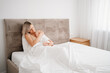 © andrey - Nude mom is sitting with a sleepy baby in a white bed after feeding breast milk.