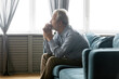 © fizkes - Side view pensive older retired man sitting on sofa, looking in distance, suffering from loneliness or having psychological problems. Unhappy middle aged grandfather lost in thoughts alone at home.