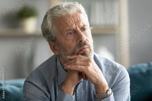 Head shot thoughtful elderly mature bearded man looking in distance, considering personal psychological problems alone at home. Unhappy pensive middle aged grandfather feeling lonely indoors.