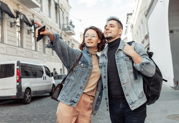 Wall Mural - Charismatic modern couple of tourists in love in denim jackets stroll along the urban street