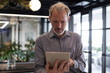 © Wavebreak Media - Caucasian businessman standing by window using digital tablet in modern office