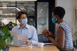 © Wavebreak Media - Diverse business people wearing face masks sitting using laptop going through paperwork in office