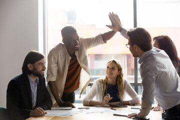 Happy young african american employee giving high five to smiling 30s male team leader at colleagues group brainstorming meeting, celebrating successful project finish or sharing corporate success.