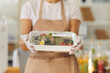 © Studio Romantic - Close up of food on takeaway plastic container in the hands of a faceless woman wearing disposable gloves. Employee gives the client a ready fresh healthy lunch. Selective focus blurred background.