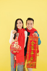 Poster - Happy young Asian couple in winter clothes showing Lunar New Year decorations with best wishes inscription